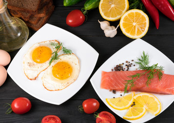 red fish, fried eggs with vegetables on a black wooden background