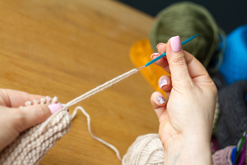 Hands of a young woman knit crochet from beigeyarn on a light wooden surface. Start a new bag of yarn.