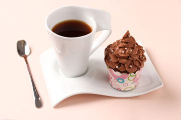 Chocolate cream cupcake and a cup of coffee arranged on a pink background