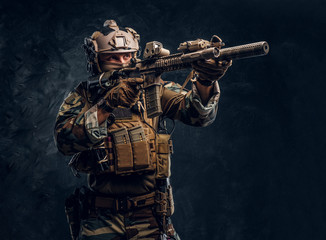 Fototapeta na wymiar Elite unit, special forces soldier in camouflage uniform holding an assault rifle with a laser sight and aims at the target.