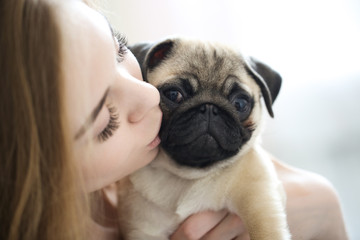 blonde girl with kisses and holds pug puppy