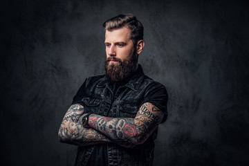 Portrait of a stylish bearded guy with tattooed hands. Studio photo against dark wall
