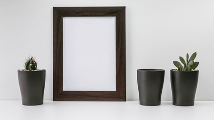 Empty dark photo frame and two succulents in dark pots on a white background. Scandinavian style MockUp