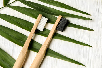 bamboo toothbrushes on white wood background with tropical leaf. Place for text. Ecoproduct.  ...