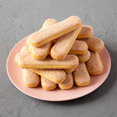 Savoyardi or ladyfingers cookies on pink plate on gray background, side view. Close-up.