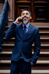 Portrait of a  happy senior businessman talking on the phone while standing outside
