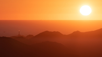 The lighthouse of Cabo de Palos and the Mediterranean Sea seen from afar behind the mountains of Calblanque at sunrise.