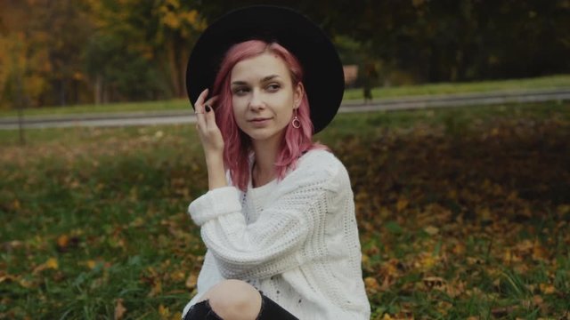 Female hipster in hat rests on the park's lawn and poses at camera