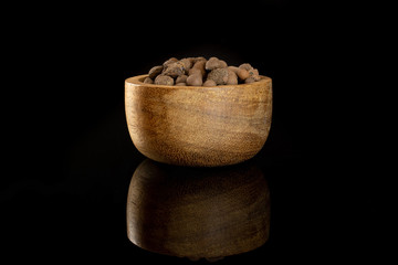 Lot of whole brown clay pebbles (leca) with wooden bowl isolated on black glass
