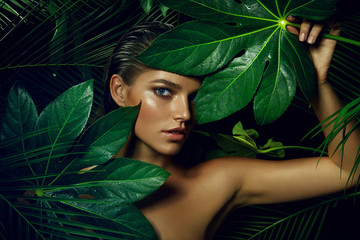Fototapeta A beautiful tanned girl with natural make-up and wet hair stands in the jungle among exotic plants. obraz