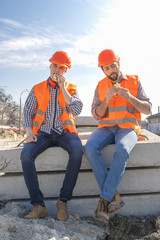 two workers in helmets lunch, rest, sit on concrete slabs