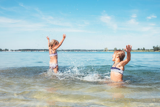 Two little sister girls fooling around in the calm sea waves splashing water to each other. Family vacation concept image.