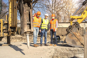 male workers engineers in helmets talking near the bulldozer and excavator