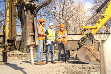 male workers engineers in helmets talking near the bulldozer and excavator