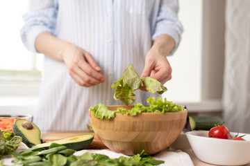 woman in a blue shirt preparing vegetable salad, lay lettuce