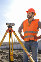 male surveyor engineer with a device working on a construction site in a helmet