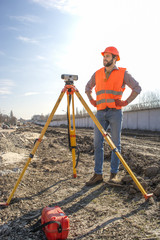 male surveyor engineer with a device working on a construction site in a helmet