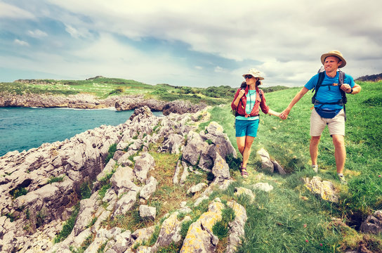 Couple backpacker travelers walk on ocean rocky coast. Asturias. Spain