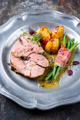 Gegrillter marinierter griechischer Lammbraten mit Kartoffel und Bohnen gerollt in Speck als closeup auf einem Zinnteller