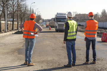 male workers engineers at a construction site with the head in helmets look at the house that is being built