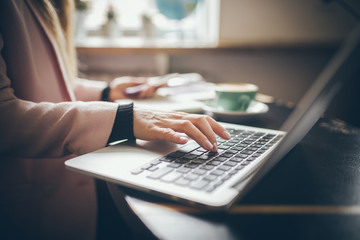 Close-up top view of Caucasian woman's hands Casually dressed student, blogger, writer man working on a laptop holding a phone in his hand, inside the cafe a wooden table and a cup of coffee