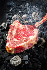 Traditional raw dry aged wagyu tomahawk steak on hot burning charcoal with smoke as closeup on a...