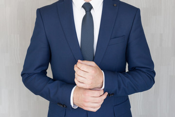 Torso of anonymous businessman wearing beautiful fashionable classic navy blue suit against grey...