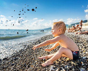 Fototapeta na wymiar Little child boy on the beach throws small stones into the water on the sea coast