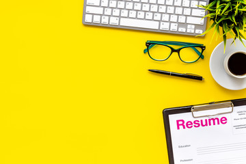 Empoyment concept with resume on yellow work desk background with coffee, glasses, keyboard top view space for text