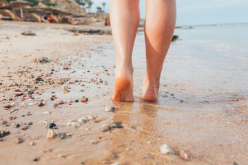Beautiful girl legs walks on the sand and sea water on the beach