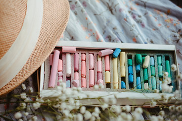 spring palette: a box of multicolored pastel crayons and a straw hat