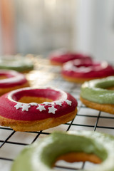 Home made baking - selective focus of fresh baked donuts with bright pink and green icing on cooling rack