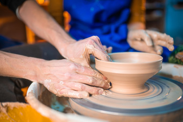 Fototapeta na wymiar Traditional pottery making, man teacher shows the basics of pottery in art studio. Artist operates hands, which gently creating correctly shaped jug handmade from clay