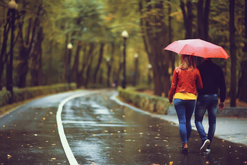 rain in the autumn park / young 25 years old couple man and woman walk under an umbrella in wet rainy weather, walk October lovers