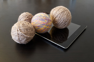 Hobby on the Internet.Gray and colored wool yarns for home knitting and tablet computer on a dark wooden table.