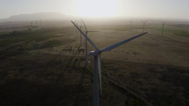 4K aerial close-up view of wind turbines turning on a wind farm at sunset