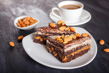 Chocolate cake with caramel, peanuts and almonds on a black wooden background.