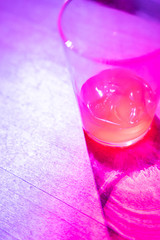 A crystal glass with pink liquid inside. It is illuminated by colored lights. Interplay of light and shadows.