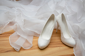 White, womens, wedding shoes with heels with patterns in the shape of flowers on the background of the wedding dress.
