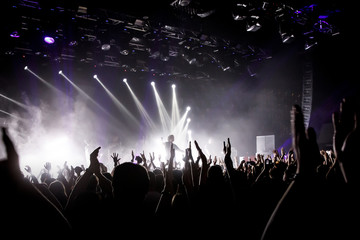 Crowd on music show, happy people with raised hands. White stage light. Frontman on stage.