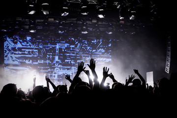 Crowd on music show, happy people with raised hands. White stage light. Frontman on stage.
