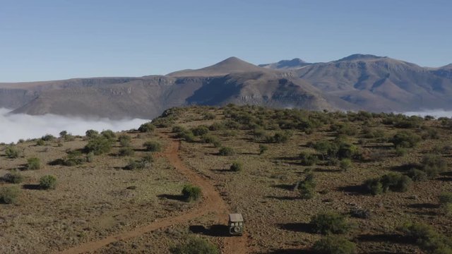 4K aerial tilit up view of a safari 4x4 game drive vehicle driving  on a gravel road beautiful mountain scenery in the background