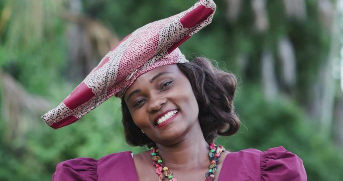 4K close-up portrait of pretty black Herero woman in Traditional Dress looking at the camera with her head tilted to one side