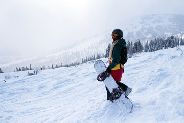 Female snowboarder freerider goes to the mountains holding a snowboard.