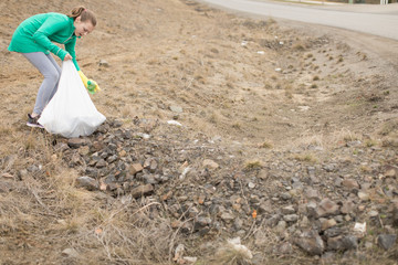 Fototapeta premium Young girl picking up litter on side of road with garbage bag