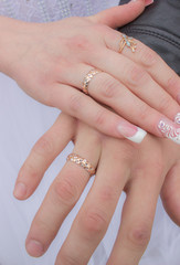 Hands with wedding rings on the nameless finger on the background of a wedding dress.