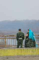 Naklejka premium Bride and groom in dress and costume in military style on the river bridge.