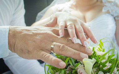 Hands of the bride and groom with a ring finger on the background of a wedding bouquet of white...