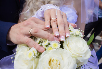 Obraz na płótnie Canvas Hands with rings on the fingers of the bride and groom on the background of a wedding bouquet with big white roses.