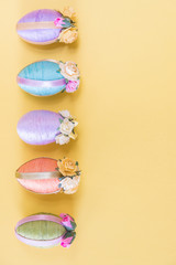 Row of vintage style multi-colored Easter eggs on sold yellow background